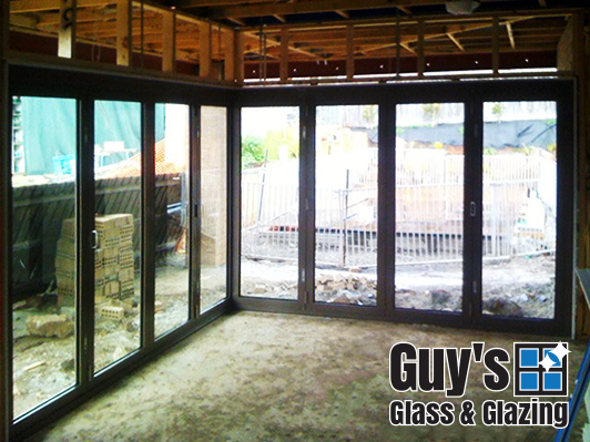 A corner set of aluminium bifold doors. Stylish and modern but also functional. The view from inside looking out with doors closed.
